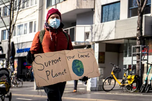 A man holds a sign at a protest reading 'Support your local planet'